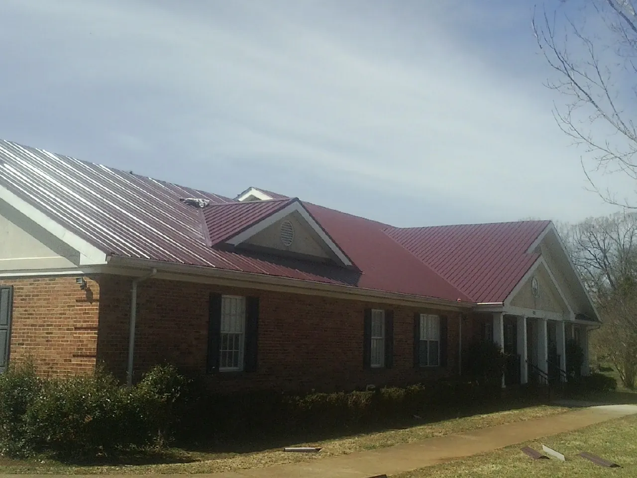 Red metal roof with gabled entries on a long brick building, from a Hail Damage Roof Repair job in Osburn