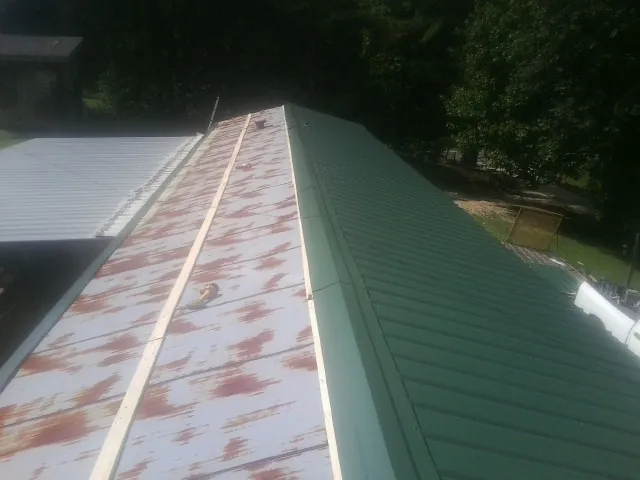 Old rusted panels beside newly installed green metal roofing — Wind Damage Roof Repair by Roofing Brothers in Osburn