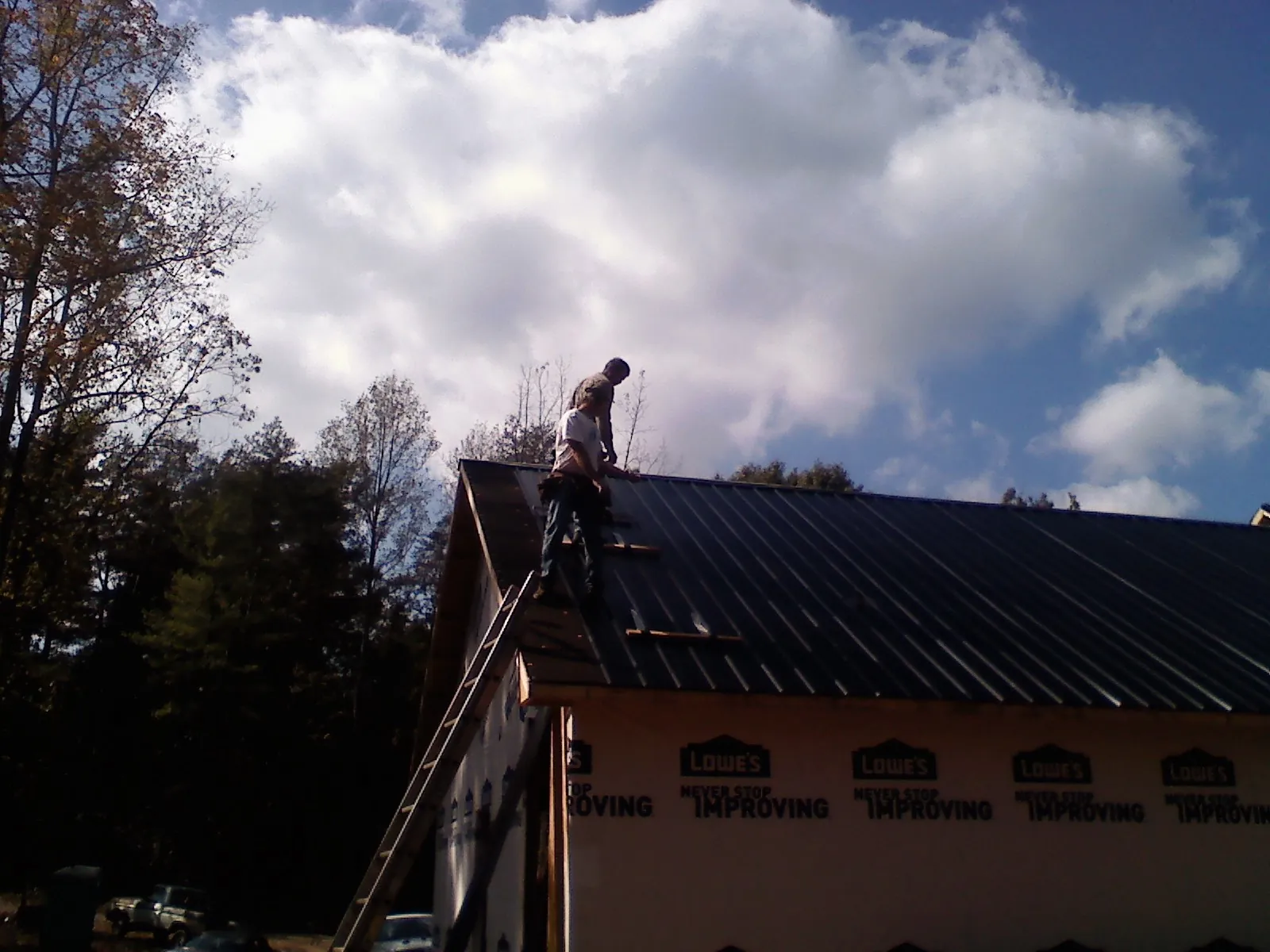 Roofer fastening dark metal panels high against a cloudy sky, from a Roof Inspection job in Osburn