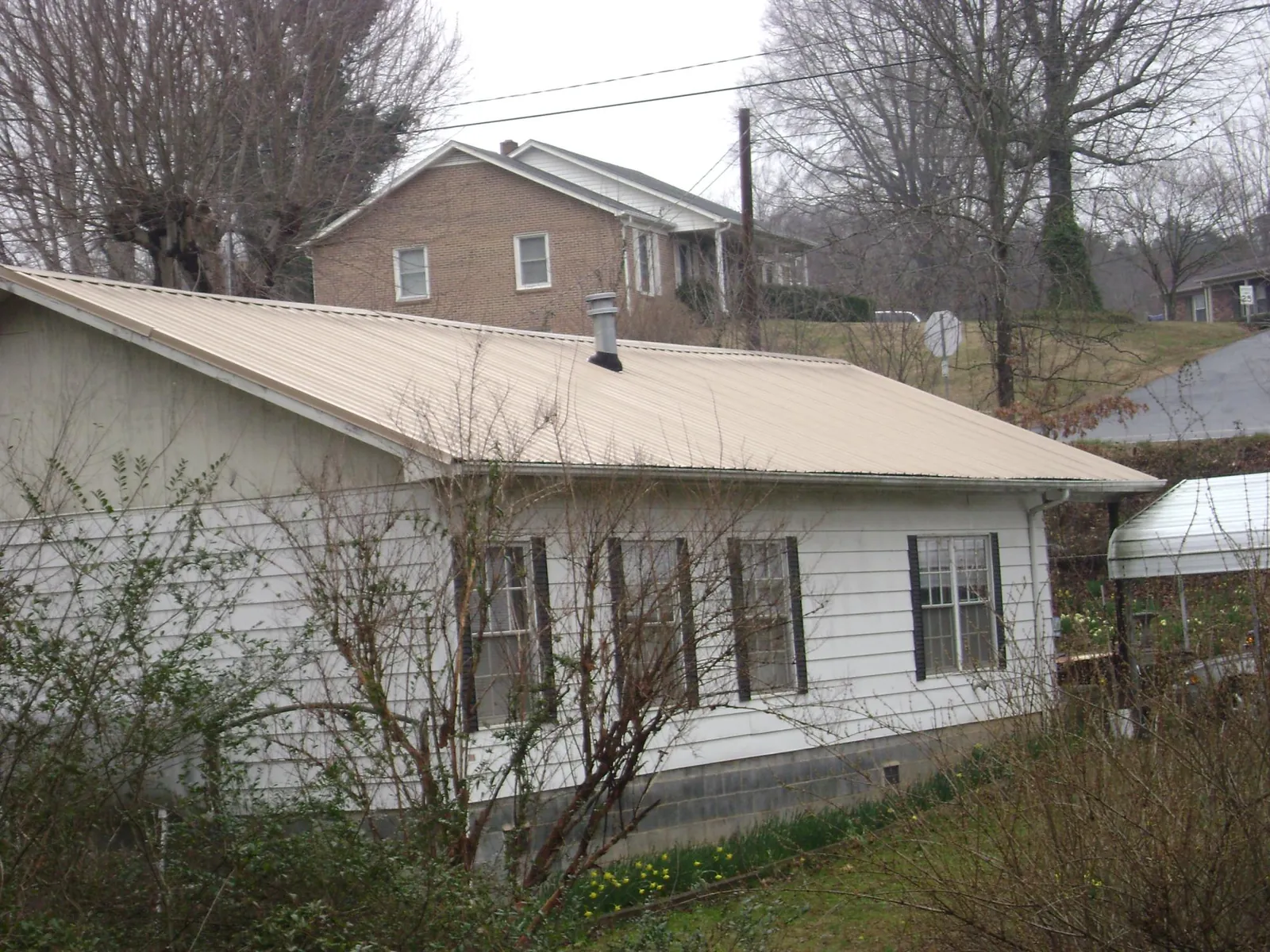 Tan metal roof on a white sided house set into a hillside — Commercial Roofing by Roofing Brothers in Osburn