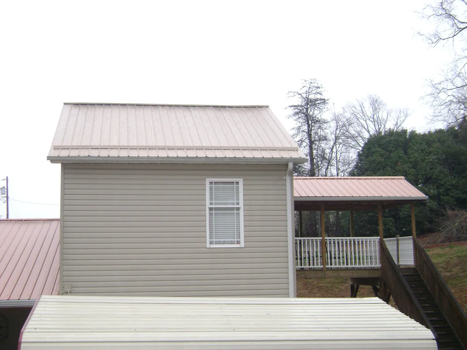 Tan metal roofs on a two story addition and attached porch, from a Roof Replacement job in Osburn